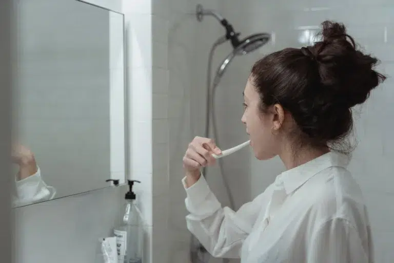 Woman brushing her teeth in bathroom mirror