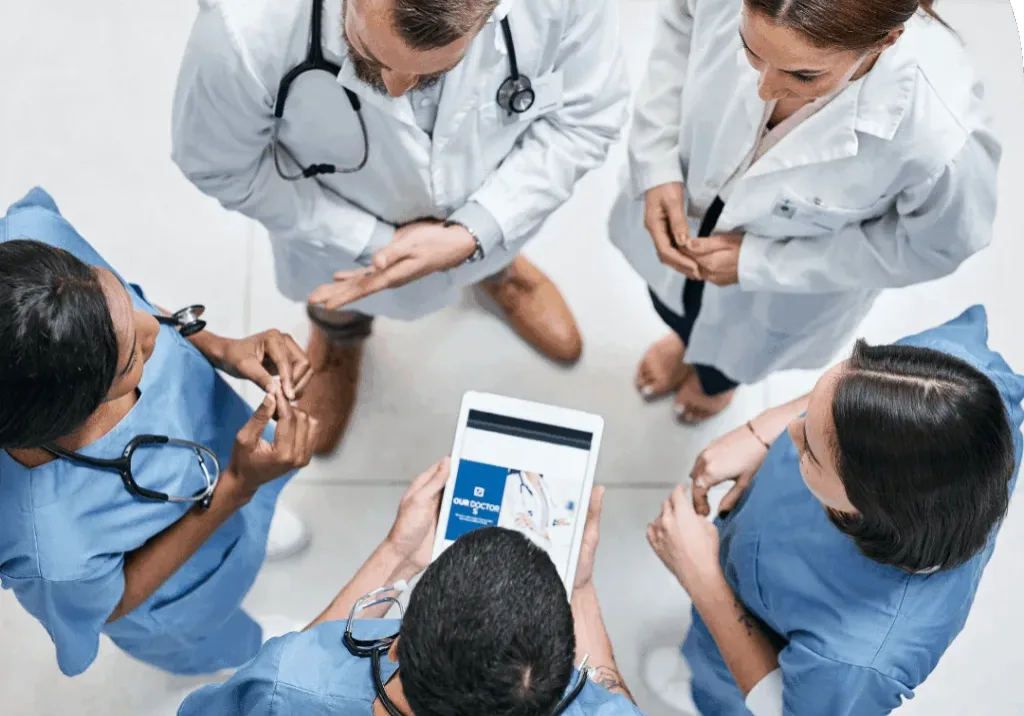 Overhead view of healthcare professionals standing together and reviewing information on a tablet during a care discussion.